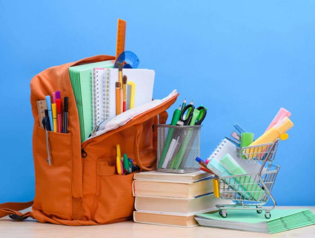 Orange school backpack full of school supplies and a supermarket basket with office supplies on a blue background (Target + Walmart Roll Out Special Deals for Teachers and Students)