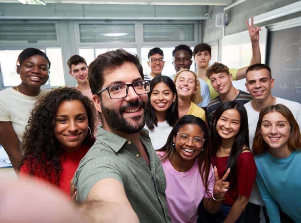 Happy selfie of young group of Erasmus students taking a photo with their teacher in the classroom.