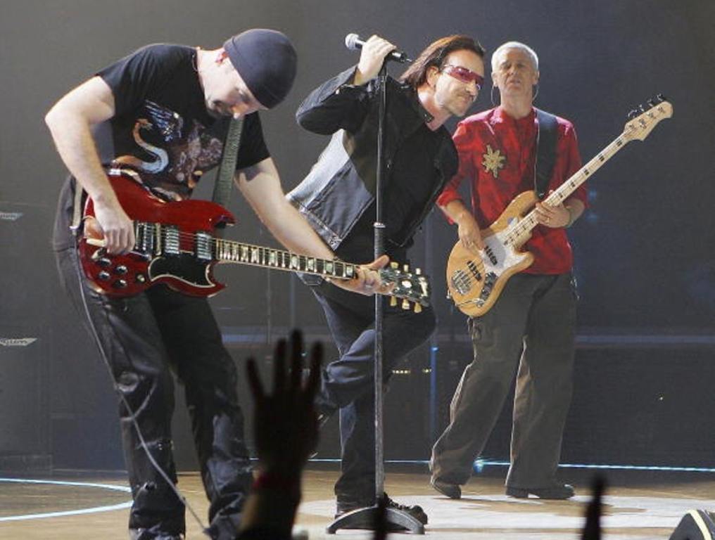 U2 performs in a surprise concert on Fremont Street. From left to right: "The Edge" on guitar, Bono on lead vocals singing into microphone, and Adam Clayton playing bass.