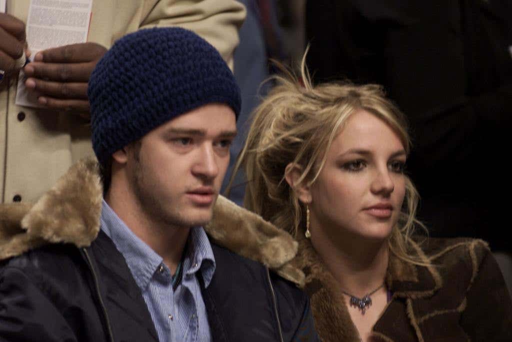 Justin Timberlake wearing a navy beanie, blue button down and black jacket and Britney Spears wearing a brown shirt with her hair tied up at the "NBA All-Star Game" looking right.