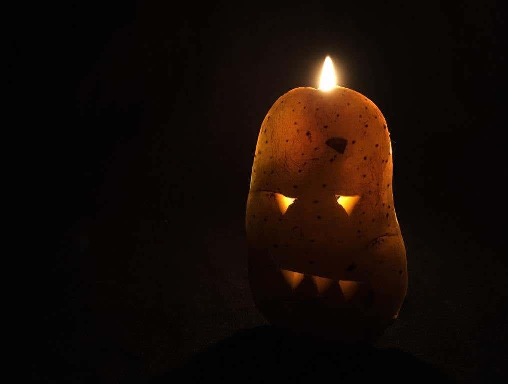 Lit potato, carved like Jack-o'-lantern with scary face. halloween potatoes concept