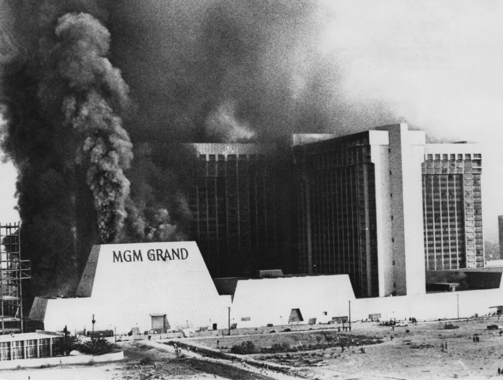 A black and white photo of the MGM fire of 1980. Enormous plumes of smoke are billowing from the casino.