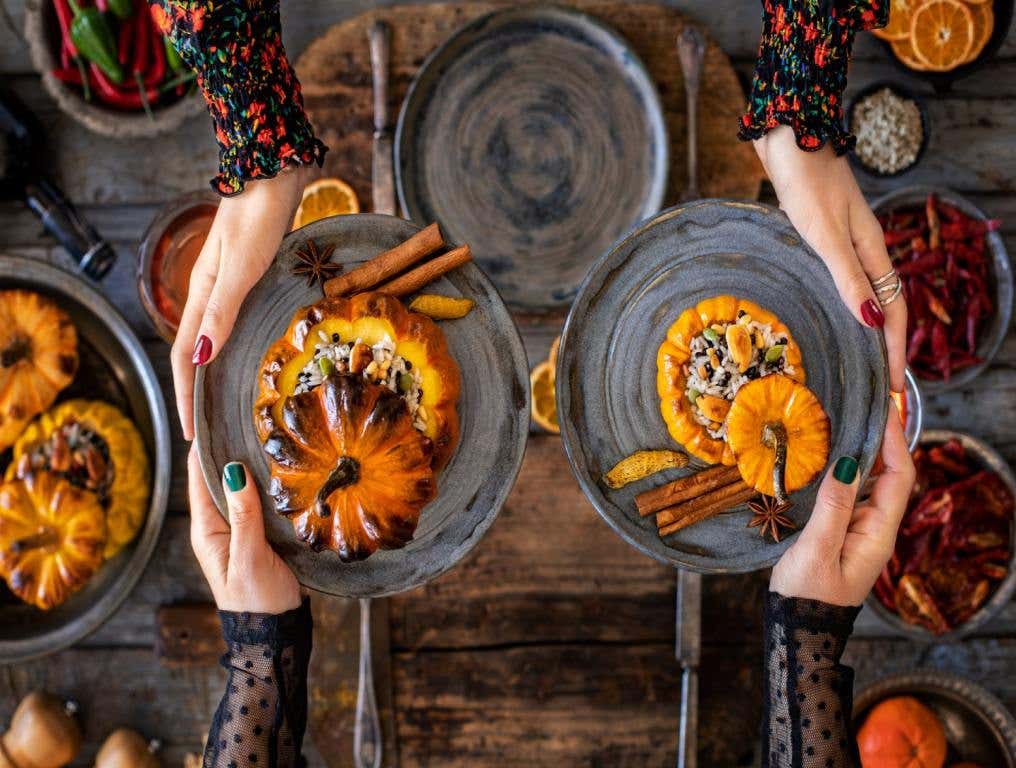 Vegan food with table top view. Mini pumpkins stuffed with rice and veggies are on plates that are being passes back and forth by two pairs of hands.