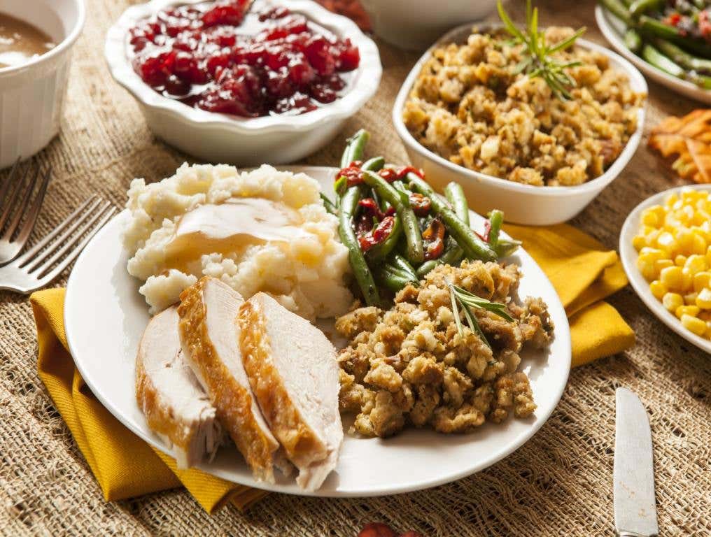 A thanksgiving meal is portioned out on a white plate. Surrounded by dishes of traditional thanksgiving side dishes.