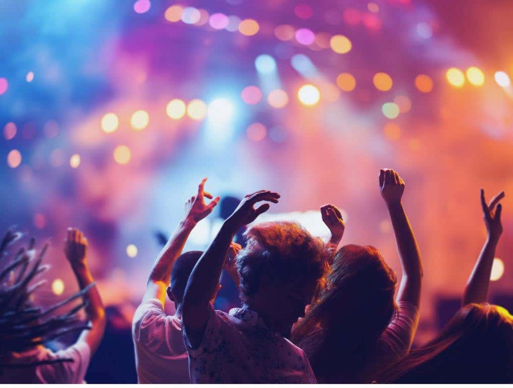 Colorful picture of concert goers, with their arms raised and their backs to us. They are enjoying the performer (not seen) at one of many summer music festivals.