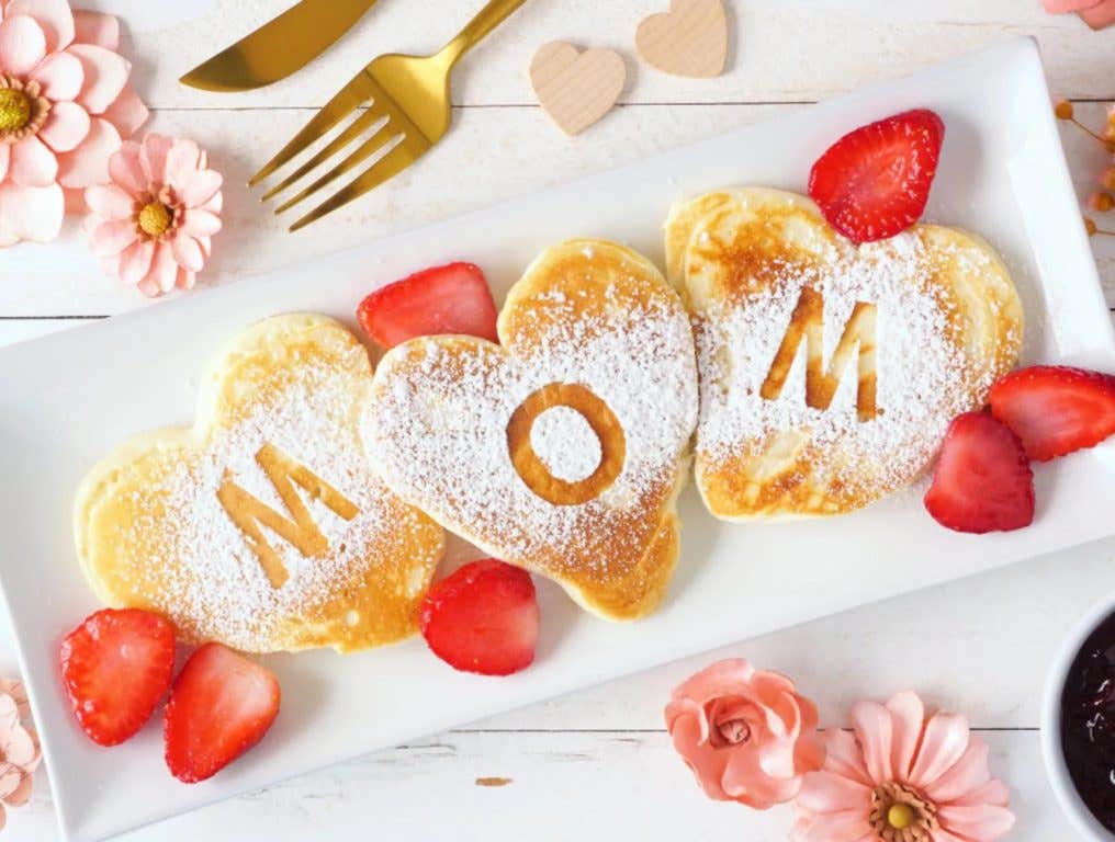 Heart shaped pancakes with MOM letters. Mothers Day breakfast concept. Top view table scene with a white wood background. Mother's Day 2024 concept.