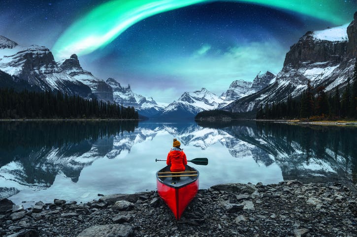 Traveler woman sitting on canoe with aurora borealis over Spirit Island in Maligne lake at Jasper national park, Alberta, Canada