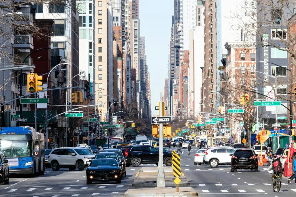 Busy street view with people, cars and buses in the crowded intersections on 3rd Avenue in the East Village neighborhood of New York City.